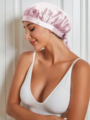 Light pink mulberry silk sleep cap with a tie-back, worn by a woman in a white top.