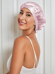 Smiling woman wearing a pink mulberry silk sleep cap with tie closure, protecting hair.