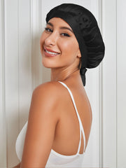 Smiling woman wearing a black mulberry silk sleep cap with a tie closure, protecting hair.