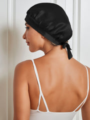 Black 100% Mulberry silk sleep cap with tie closure on a woman, protecting hair from frizz.