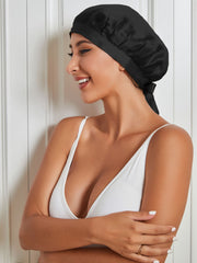 Smiling woman wearing a black mulberry silk sleep cap with a tie closure, protecting hair.