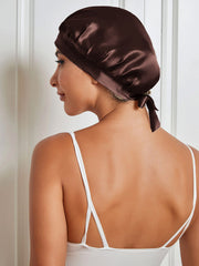 Woman wearing a dark brown 100% mulberry silk sleep cap with a tie closure, protecting hair.
