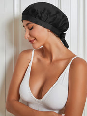 Woman wearing a black mulberry silk sleep cap with a tie closure, over a white ribbed top.