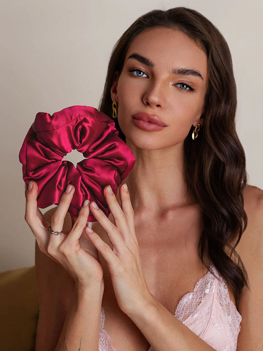 Woman holding a large, soft mulberry silk scrunchie in a rich magenta color.