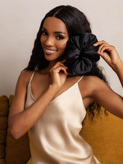 Smiling woman holding a large black mulberry silk scrunchie, 8cm, against her cheek.