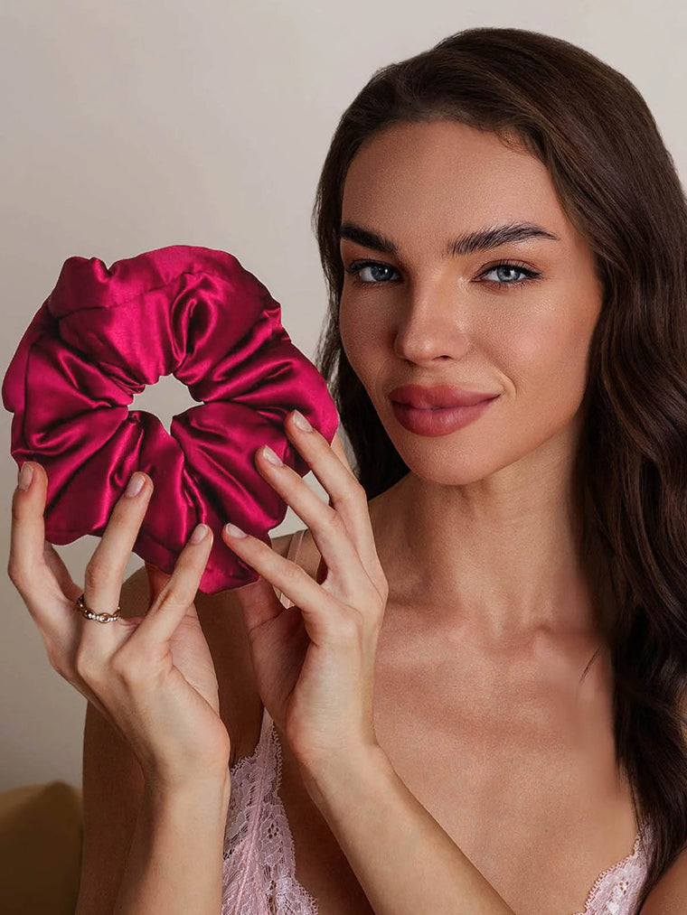 Woman holding a wine-colored, oversized mulberry silk scrunchie, showcasing its soft, luxurious texture.