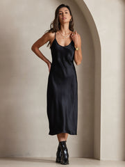 Black mulberry silk spaghetti strap midi dress on a woman, paired with black boots.