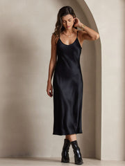 Women's black mulberry silk spaghetti strap midi dress with a subtle sheen, worn with black boots.