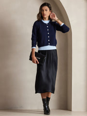 Woman in black silk midi skirt, navy cardigan with light blue trim, and black clutch.