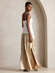 Woman wearing a white mulberry silk spaghetti strap camisole top and gold silk wide-leg pants.