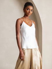 Woman wearing a white mulberry silk spaghetti strap V-neck camisole top with gold pants.