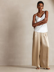 Woman in a white mulberry silk spaghetti strap camisole top and gold wide-leg silk pants.