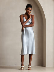 Woman in a light blue mulberry silk spaghetti strap V-neck midi dress with criss-cross back design.