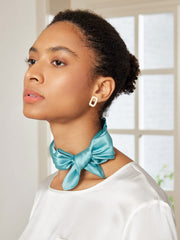 Woman wearing a teal mulberry silk square scarf tied in a bow around her neck.