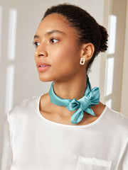 Woman wearing a teal mulberry silk square scarf tied around her neck with a white silk top.