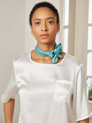 Woman wearing a teal mulberry silk square scarf tied around her neck with a white silk top.