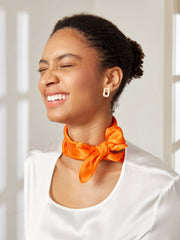 Smiling woman wearing an orange mulberry silk square scarf tied around her neck.