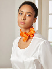 Woman wearing a vibrant orange mulberry silk square scarf tied around her neck with a white silk top.