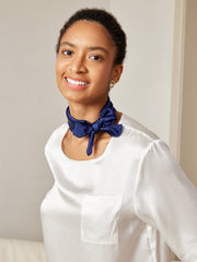Smiling woman wearing a navy blue mulberry silk square scarf tied around her neck with a white silk top.