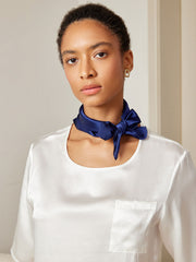 Woman wearing a navy blue 100% mulberry silk square scarf tied around her neck with a white silk top.