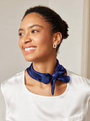 Woman wearing a navy blue 100% mulberry silk square scarf tied around her neck.