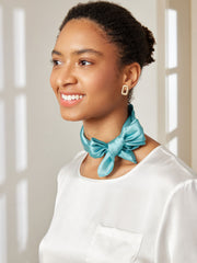 Smiling woman wearing a teal mulberry silk square scarf tied in a bow, with a white silk top.