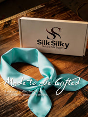 Aqua 100% Mulberry silk square scarf, 53x53cm, tied in a knot, with a white gift box on a wooden surface.