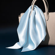 Light blue 100% mulberry silk square scarf, 53x53cm, draped on a beige handbag.