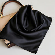 Black 100% mulberry silk square scarf, 53x53cm, draped on a beige handbag.