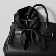 Black 100% Mulberry silk square scarf tied in a bow on a black textured handbag.
