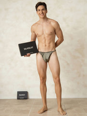 Smiling man in olive green mulberry silk string men's underwear, holding a black box.