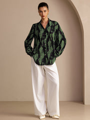 Women's mulberry silk lapel collar blouse in black and green abstract print, paired with white wide-leg pants.