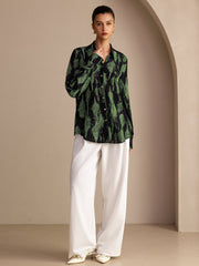 Women's mulberry silk lapel collar blouse in black with green abstract print, paired with white wide-leg pants.