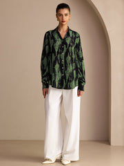 Women's mulberry silk lapel collar blouse in black with green abstract print, paired with white wide-leg pants.