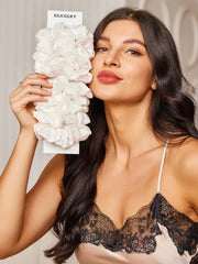 Woman holding a bundle of 10 pure white silk scrunchies, 2cm wide, with a ruffled design.