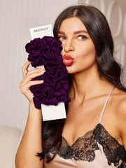 Woman holding deep purple pure silk scrunchies, showcasing their luxurious texture and classic style.