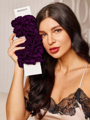 Woman holding a bundle of 10 pure mulberry silk scrunchies in a rich purple color.