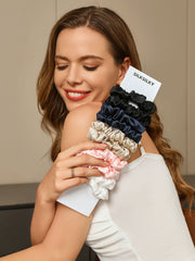 Woman holding a bundle of pure mulberry silk scrunchies in black, navy, champagne, pink, and white.