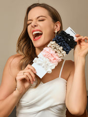 Woman holding a bundle of 10 pure mulberry silk scrunchies in black, navy, beige, pink, and white.