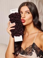 Woman holding a bundle of brown pure silk scrunchies, puckering her lips.