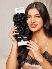 Smiling woman holding a bundle of black pure silk large hair scrunchies, 3.5cm, in a natural style.