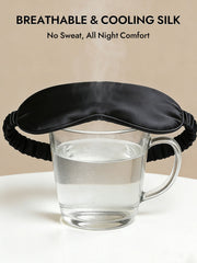 Black 19 momme pure mulberry silk sleep eye mask with elastic band over a glass of water.