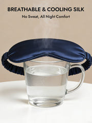Navy 19 Momme pure mulberry silk sleep eye mask with elastic band over a glass of water.
