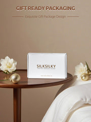 White gift box for a mulberry silk pillowcase, with flowers and ornaments on a wooden table.