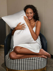 Smiling woman in a white silk nightgown hugging a luxurious white mulberry silk pillowcase.