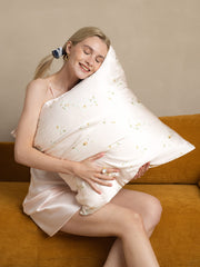 Blonde woman in silk slip hugging a Snowbud Lily 19Momme mulberry silk pillowcase with delicate floral pattern.