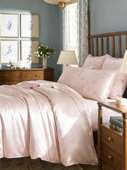 Snowbud Lily pink 19 Momme mulberry silk pillowcase and duvet cover set on a wooden bed.