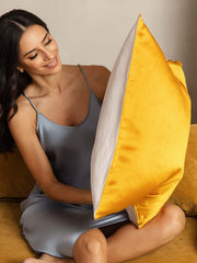 Two-tone mulberry silk pillowcase in golden yellow and white, held by a woman in a silk nightgown.