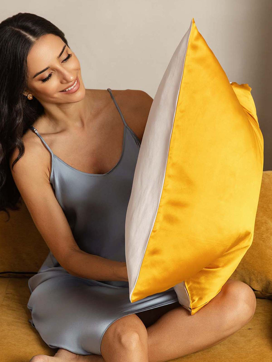 Two-tone mulberry silk pillowcase in golden yellow and white, held by a woman in a silk nightgown.
