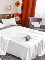 White 19 Momme mulberry silk flat sheet and two pillowcases on a bed, with two gift boxes.